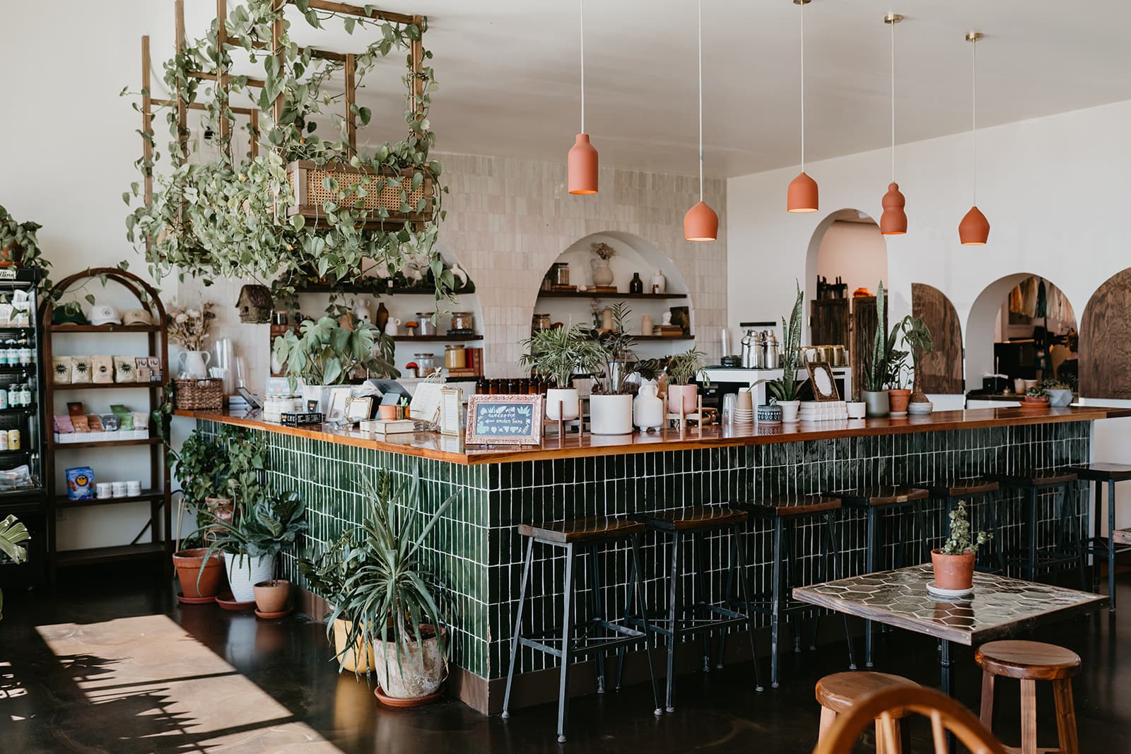 Inside Greenhouse: the corner of the green-tiled bar wrapped in hanging plants, terracotta pendant lights overhead