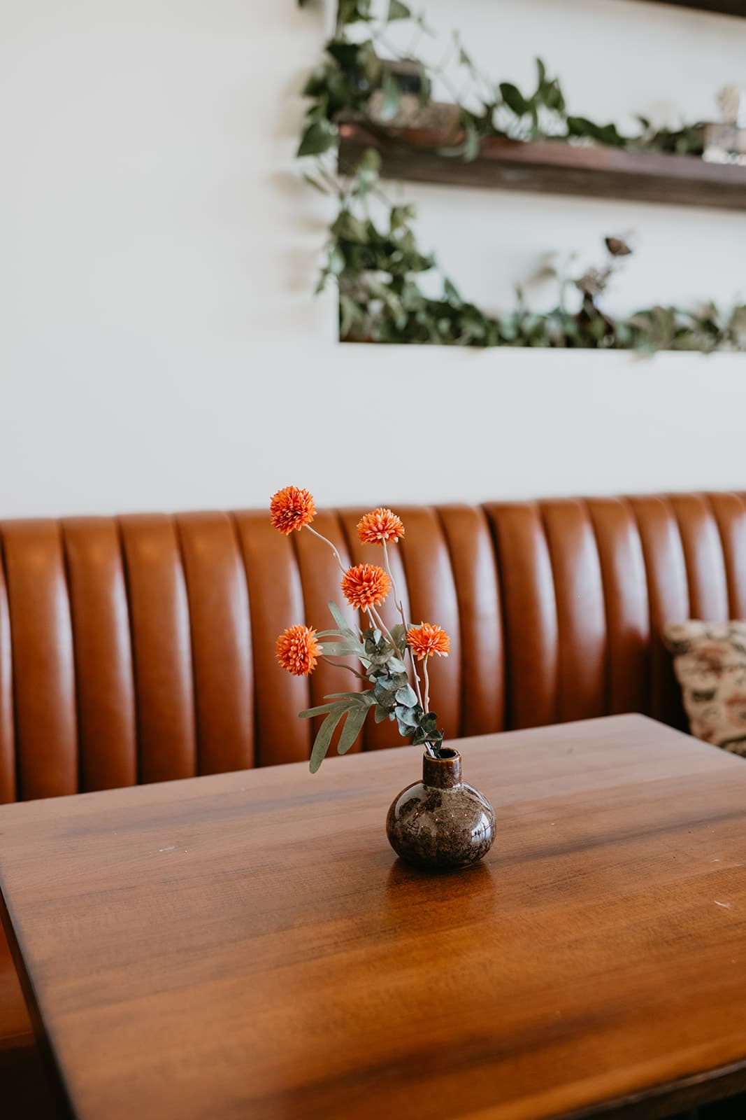Orange blooms in a bud vase on a table beside the leather banquette